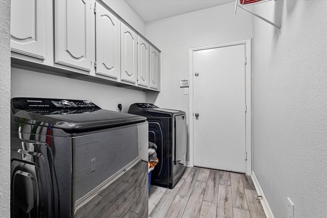 washroom with washing machine and clothes dryer, cabinet space, a textured wall, baseboards, and light wood-type flooring