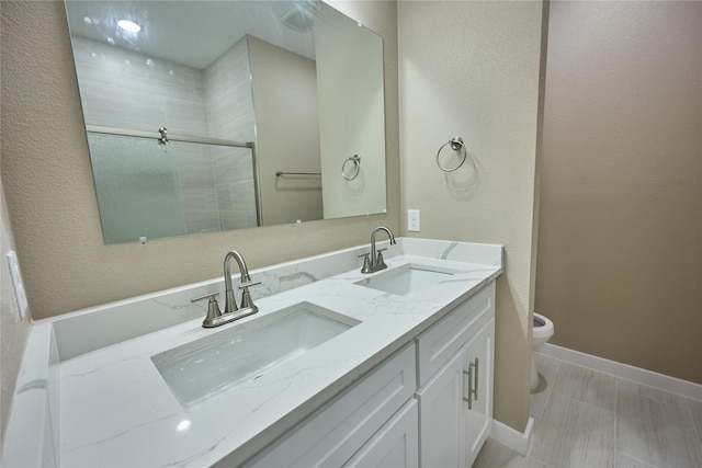 bathroom featuring a shower stall, toilet, double vanity, and baseboards