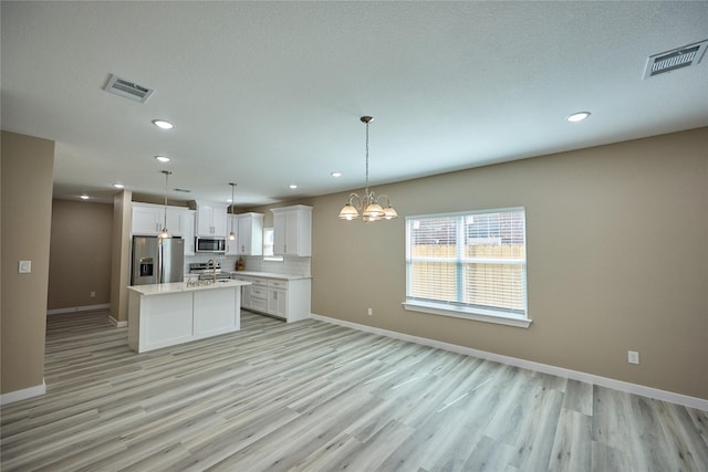 kitchen featuring appliances with stainless steel finishes, open floor plan, a center island with sink, light countertops, and recessed lighting