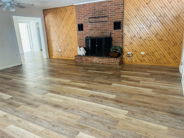unfurnished living room featuring ceiling fan, a fireplace, wood finished floors, baseboards, and wooden walls
