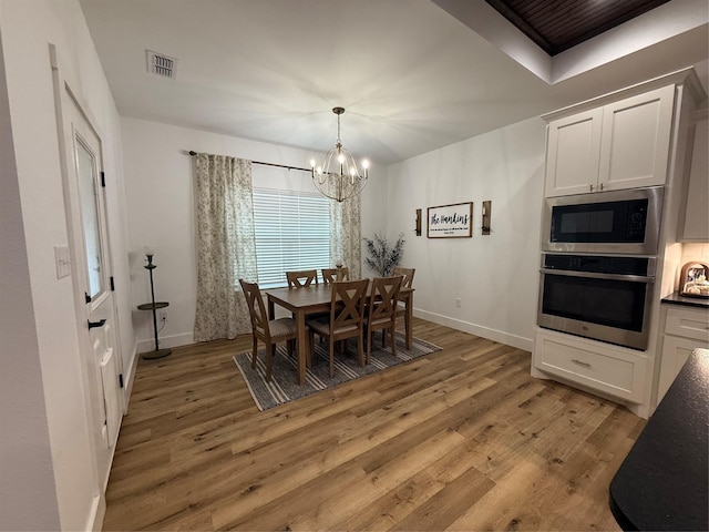 dining area with visible vents, light wood-style floors, baseboards, and an inviting chandelier