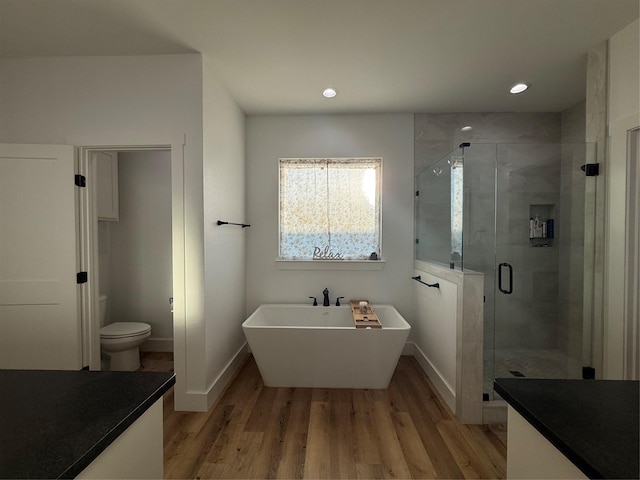 bathroom with a soaking tub, a shower stall, toilet, and wood finished floors