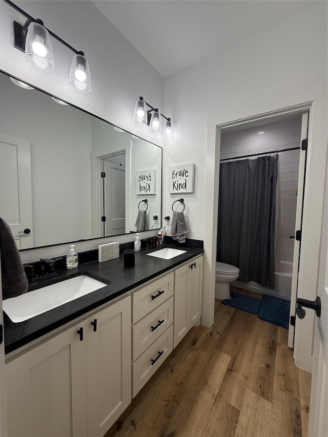 bathroom featuring toilet, double vanity, wood finished floors, and shower / tub combo