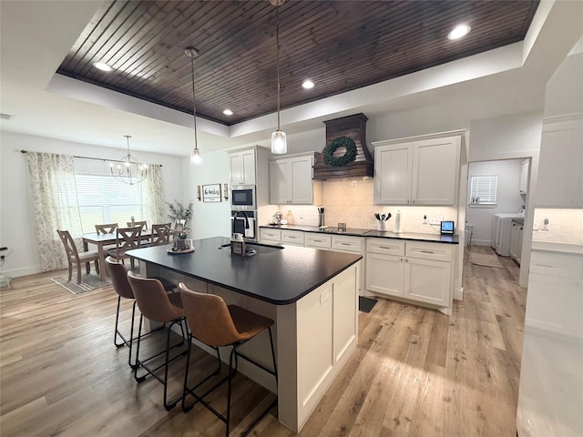 kitchen featuring dark countertops, washer and clothes dryer, a tray ceiling, wooden ceiling, and custom range hood