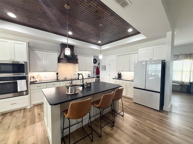 kitchen featuring dark countertops, appliances with stainless steel finishes, a sink, premium range hood, and a tray ceiling