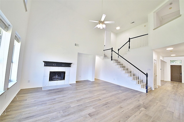 2328 Twilight Star Dr, Little Elm, TX 75068 - unfurnished living room with a towering ceiling, light wood-type flooring, stairway, a ceiling fan, and a tiled fireplace
