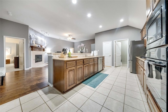 10312 Flat Creek Trl, Mckinney, TX 75072 - kitchen featuring a kitchen island with sink, a ceiling fan, appliances with stainless steel finishes, a fireplace, and brown cabinets