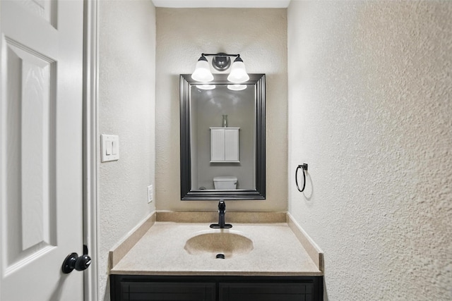 half bath with vanity, a textured wall, and toilet