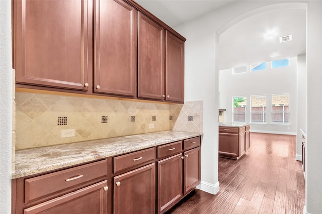 3020 Nyala Trl, Frisco, TX 75034 - kitchen with light stone countertops, arched walkways, decorative backsplash, visible vents, and dark wood-style floors
