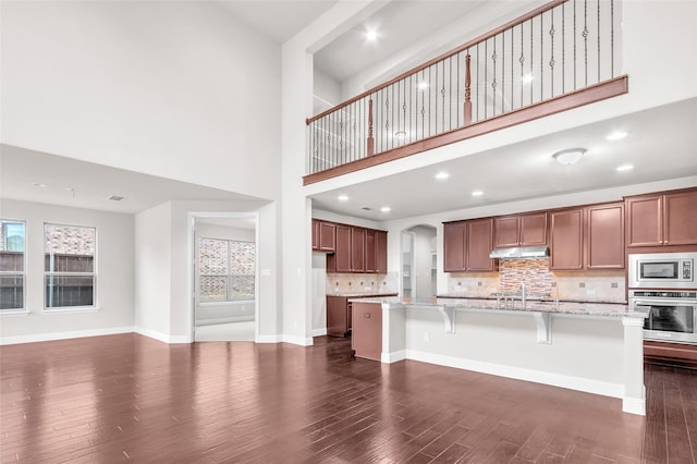 3020 Nyala Trl, Frisco, TX 75034 - kitchen featuring light stone counters, dark wood finished floors, stainless steel appliances, tasteful backsplash, and under cabinet range hood