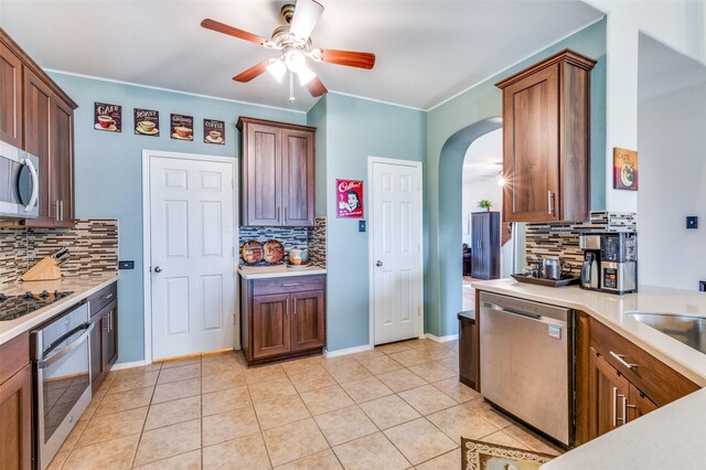 kitchen with ceiling fan, appliances with stainless steel finishes, tasteful backsplash, arched walkways, and light countertops