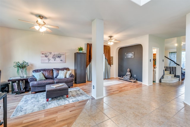 living room featuring arched walkways, ceiling fan, light tile patterned flooring, and stairway