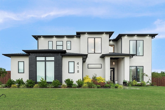 rear view of house featuring a yard, fence, and stucco siding
