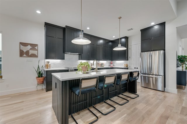 kitchen featuring dark cabinetry, freestanding refrigerator, decorative light fixtures, light wood-type flooring, and backsplash