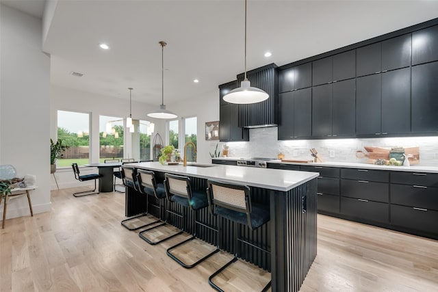 kitchen featuring light countertops, tasteful backsplash, a kitchen island with sink, and a kitchen bar