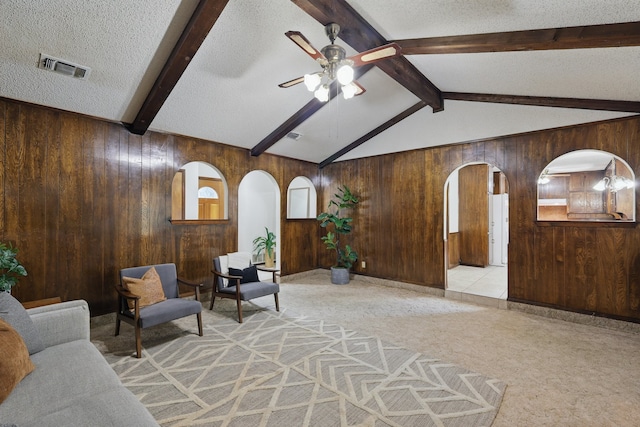 living area featuring wooden walls, arched walkways, a ceiling fan, and a textured ceiling