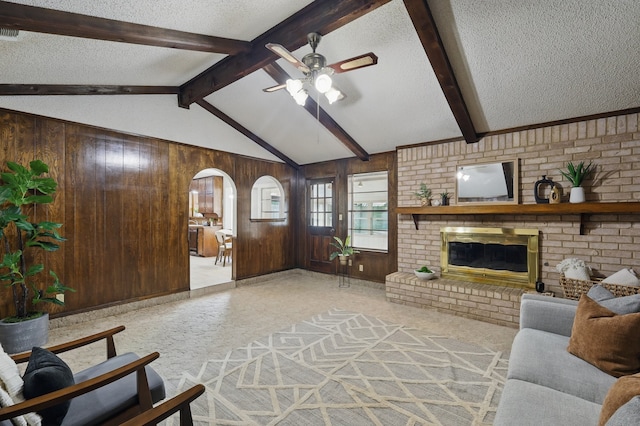 living area featuring a textured ceiling, a ceiling fan, a fireplace, wood walls, and arched walkways