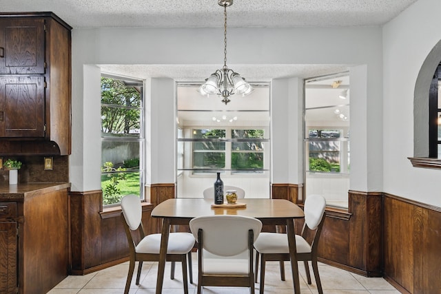 dining space featuring a wainscoted wall, light tile patterned floors, plenty of natural light, a chandelier, and a textured ceiling