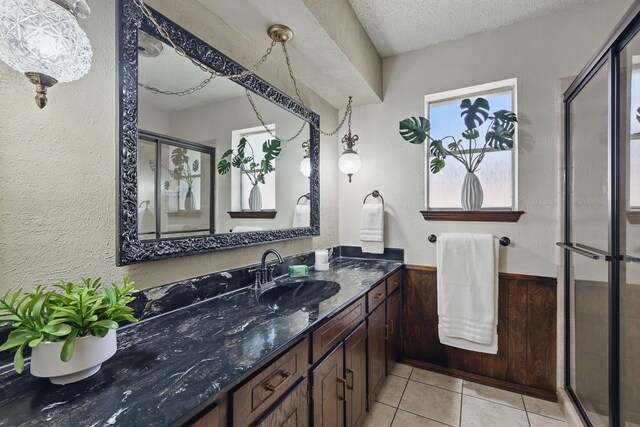 full bath with vanity, wainscoting, a stall shower, a textured ceiling, and tile patterned flooring
