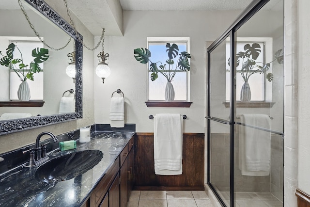 full bath featuring a shower stall, vanity, tile patterned floors, a textured ceiling, and wainscoting