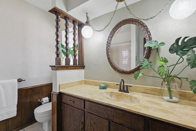 half bath with toilet, a wainscoted wall, and vanity