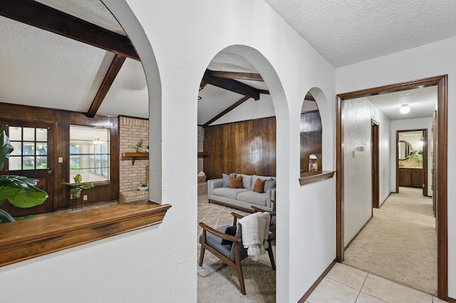 corridor featuring a textured ceiling, light carpet, light tile patterned flooring, and wooden walls