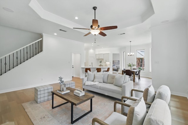 living area with a raised ceiling, ceiling fan, stairs, light wood-style floors, and recessed lighting
