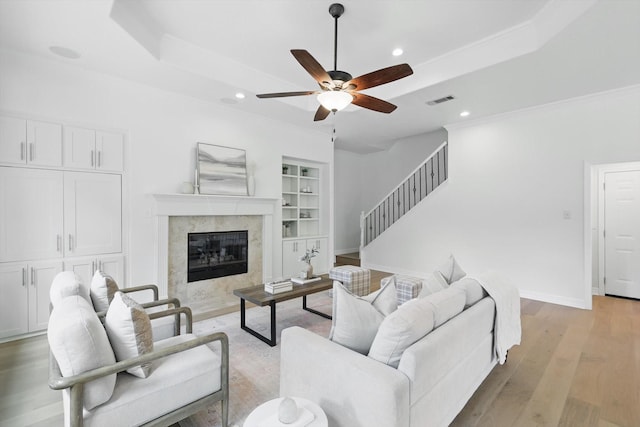living room featuring a ceiling fan, light wood-type flooring, a raised ceiling, recessed lighting, and stairway