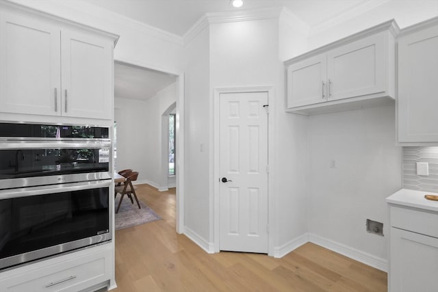 kitchen with stainless steel double oven, light wood-type flooring, decorative backsplash, baseboards, and ornamental molding
