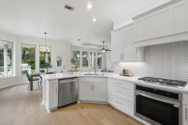 kitchen featuring stainless steel appliances, a sink, a peninsula, backsplash, and light countertops