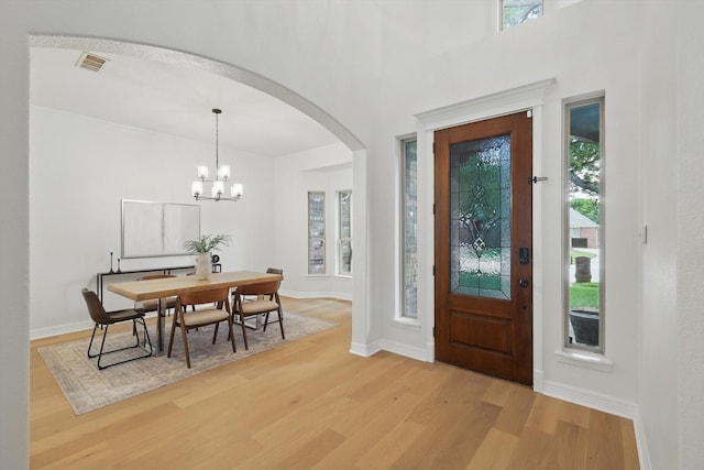 entrance foyer with arched walkways, light wood-type flooring, plenty of natural light, and a chandelier