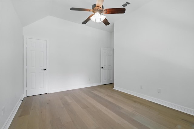 empty room with light wood-type flooring, a ceiling fan, vaulted ceiling, and baseboards
