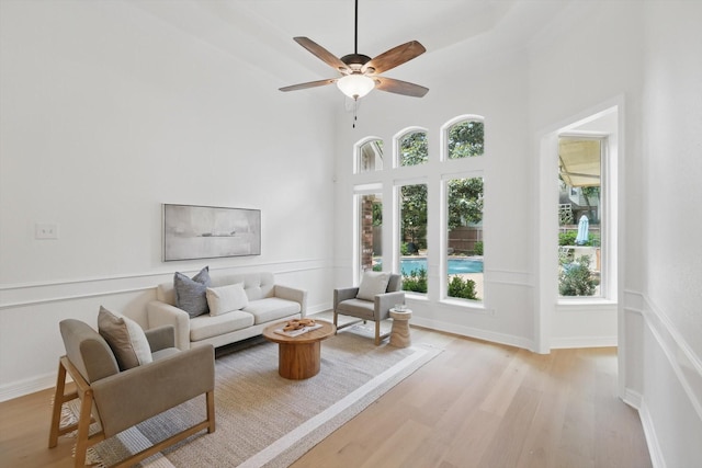 living area featuring light wood-style floors, ceiling fan, and a towering ceiling