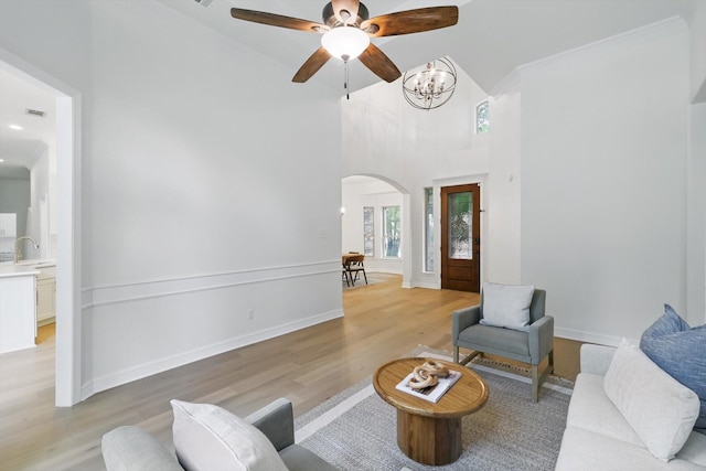 living room featuring arched walkways, light wood-style flooring, a ceiling fan, high vaulted ceiling, and a chandelier