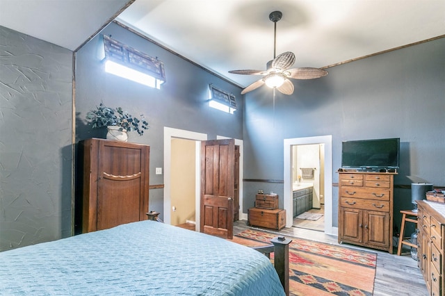 bedroom with connected bathroom, light wood finished floors, a ceiling fan, and a high ceiling