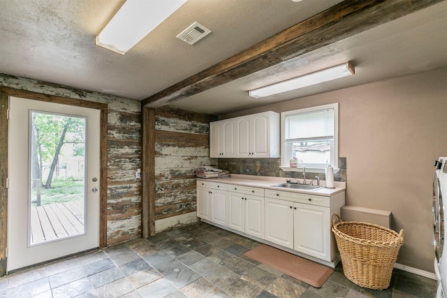 kitchen with stone finish flooring, white cabinetry, visible vents, and a sink