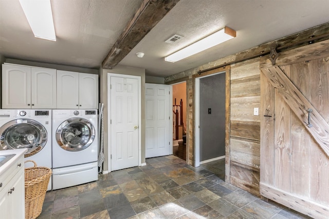 washroom with visible vents, washing machine and dryer, a barn door, cabinet space, and stone finish flooring