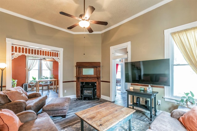 living room featuring a ceiling fan, a textured ceiling, crown molding, a wood stove, and wood finished floors