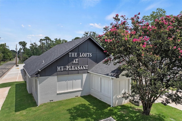 view of side of home featuring brick siding, a shingled roof, and a yard