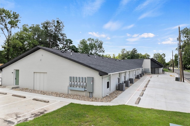 view of side of home featuring a shingled roof, cooling unit, uncovered parking, and brick siding