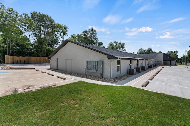view of home's exterior with uncovered parking, fence, brick siding, a lawn, and central air condition unit