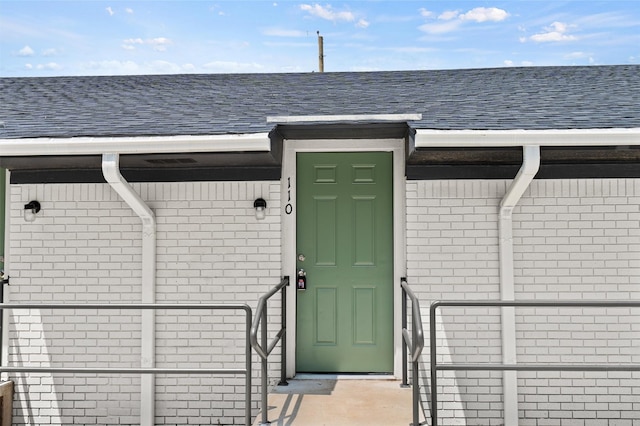 entrance to property featuring brick siding and roof with shingles