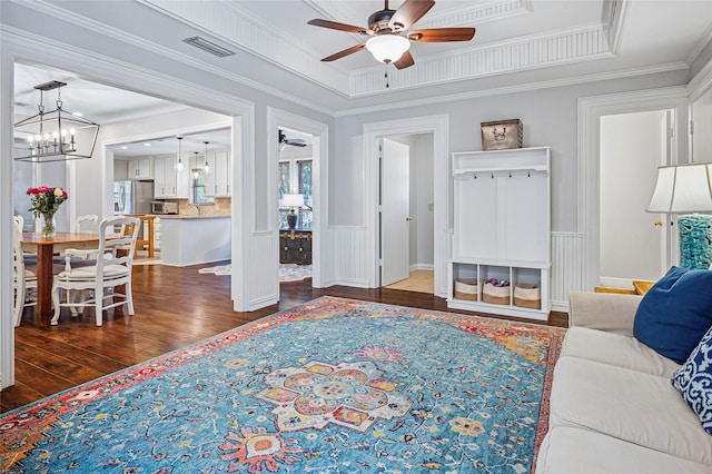 living room with ceiling fan, dark wood-style flooring, crown molding, wainscoting, and a chandelier