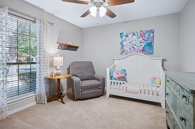 carpeted bedroom featuring a crib, baseboards, and ceiling fan