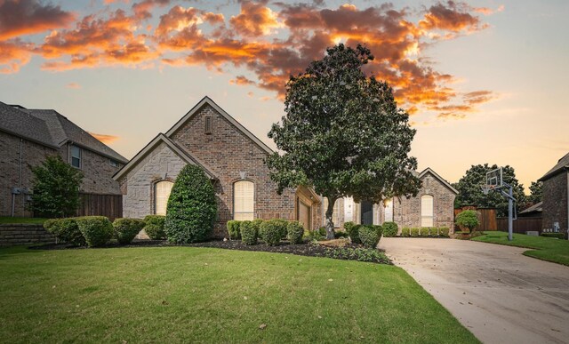 french provincial home with fence, an attached garage, brick siding, concrete driveway, and a yard
