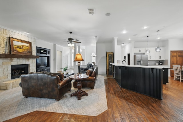 living area featuring ceiling fan, a stone fireplace, visible vents, ornamental molding, and dark wood-type flooring