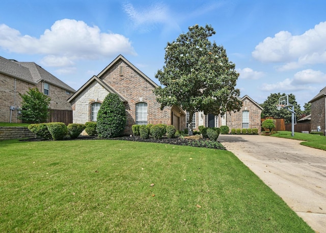 french country home featuring fence, driveway, a front lawn, and brick siding