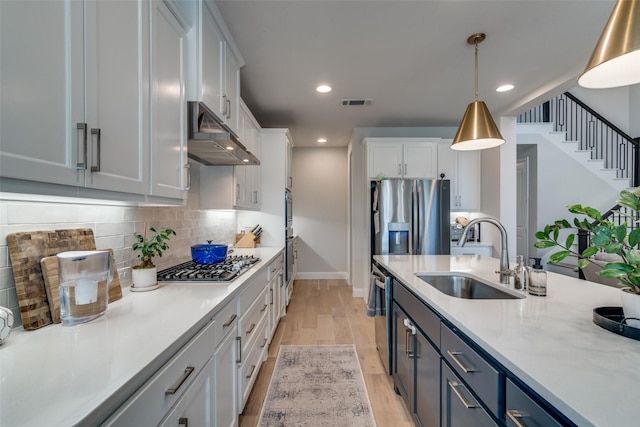kitchen featuring white cabinets, a sink, stainless steel appliances, baseboards, and under cabinet range hood