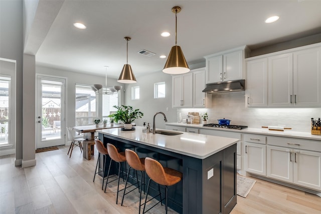 kitchen featuring a sink, backsplash, stainless steel gas stovetop, under cabinet range hood, and visible vents
