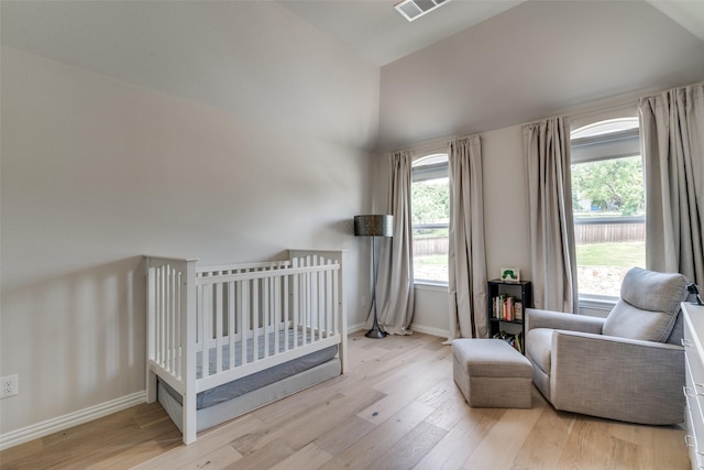 bedroom with light wood-style floors, baseboards, a nursery area, and lofted ceiling